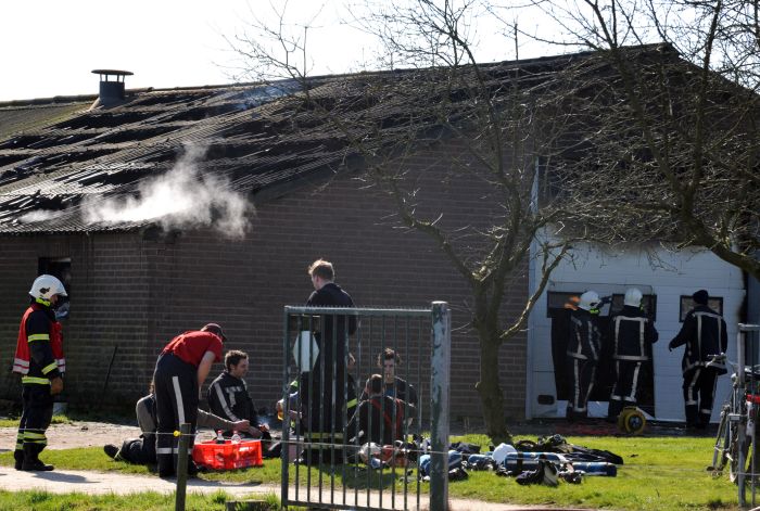 Terwijl op de achtergrond de brand nog nasmeult rusten brandweerlieden even uit na de brand in de varkensstal in Vortum-Mullem. Foto: Ed van Alem